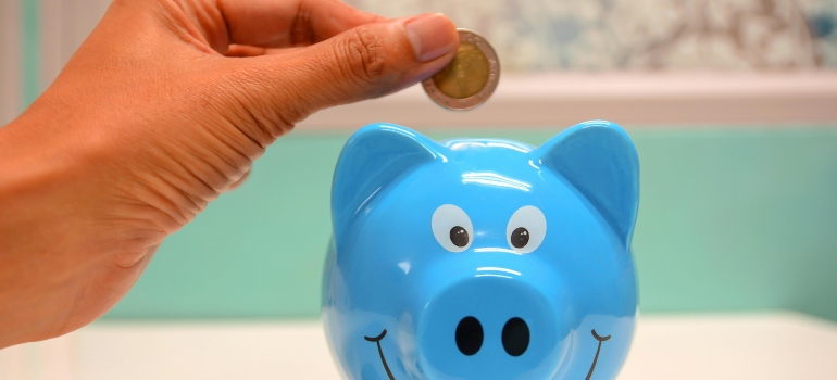 A person is putting a coin into a blue piggy bank.
