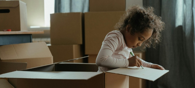 A child sitting inside a moving box while carefully drawing on its surface.