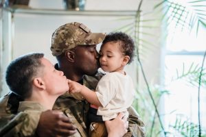 A man in military uniform is kissing his child after moving to California with the military.