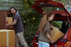 Couple carrying cardboard boxes outside near a moving truck in daylight