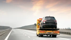 A black SUV car being professionally transported on the back of a truck driving on the highway.