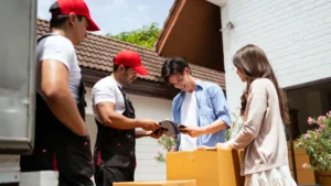 Couple signs a moving fees contract while professional movers load a moving truck with their household belongings.