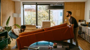 A man and a women lift a rust-colored couch so they can move into a new house.