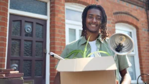 Young man holding a moving box smiles as he moves into a new urban apartment.