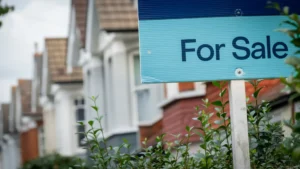 A blue sign is in front of a house advertising that it is currently for sale.