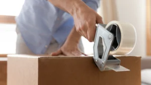 Young man packs belongings in a brown cardboard moving box as he prepares for his upcoming PCS move.