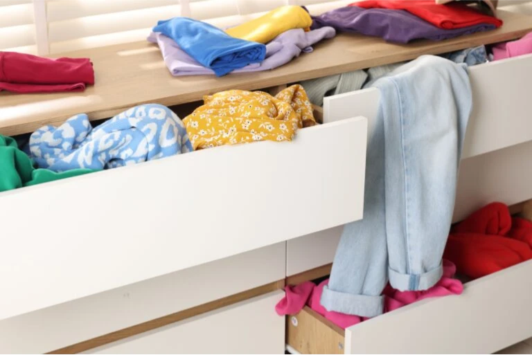 A cluttered chest of drawers in need of organization overflowing with clothing items.